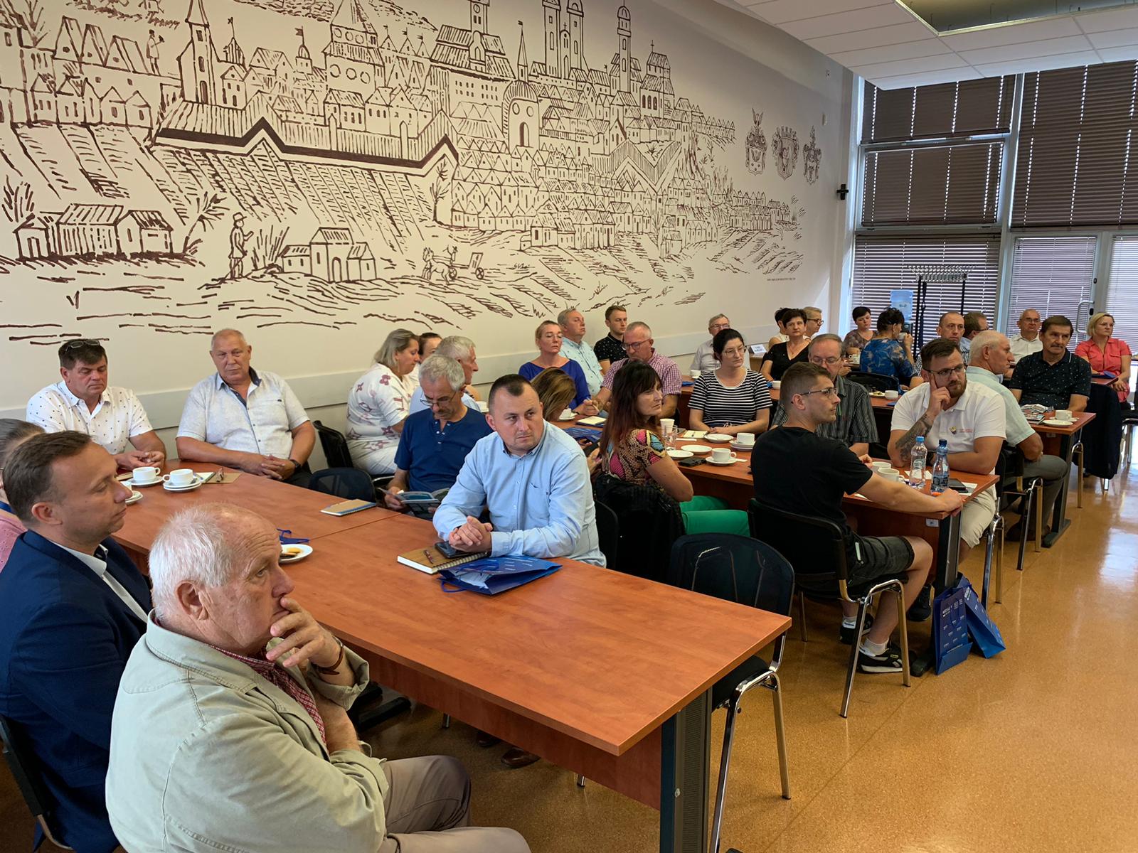 Uczestnicy szkolenia siedzą przy stołach i słuchają.