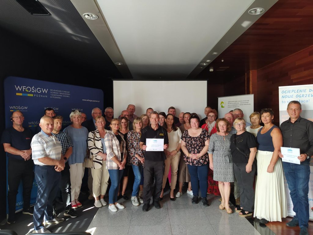 Grupa osób stoi na tle ściany.