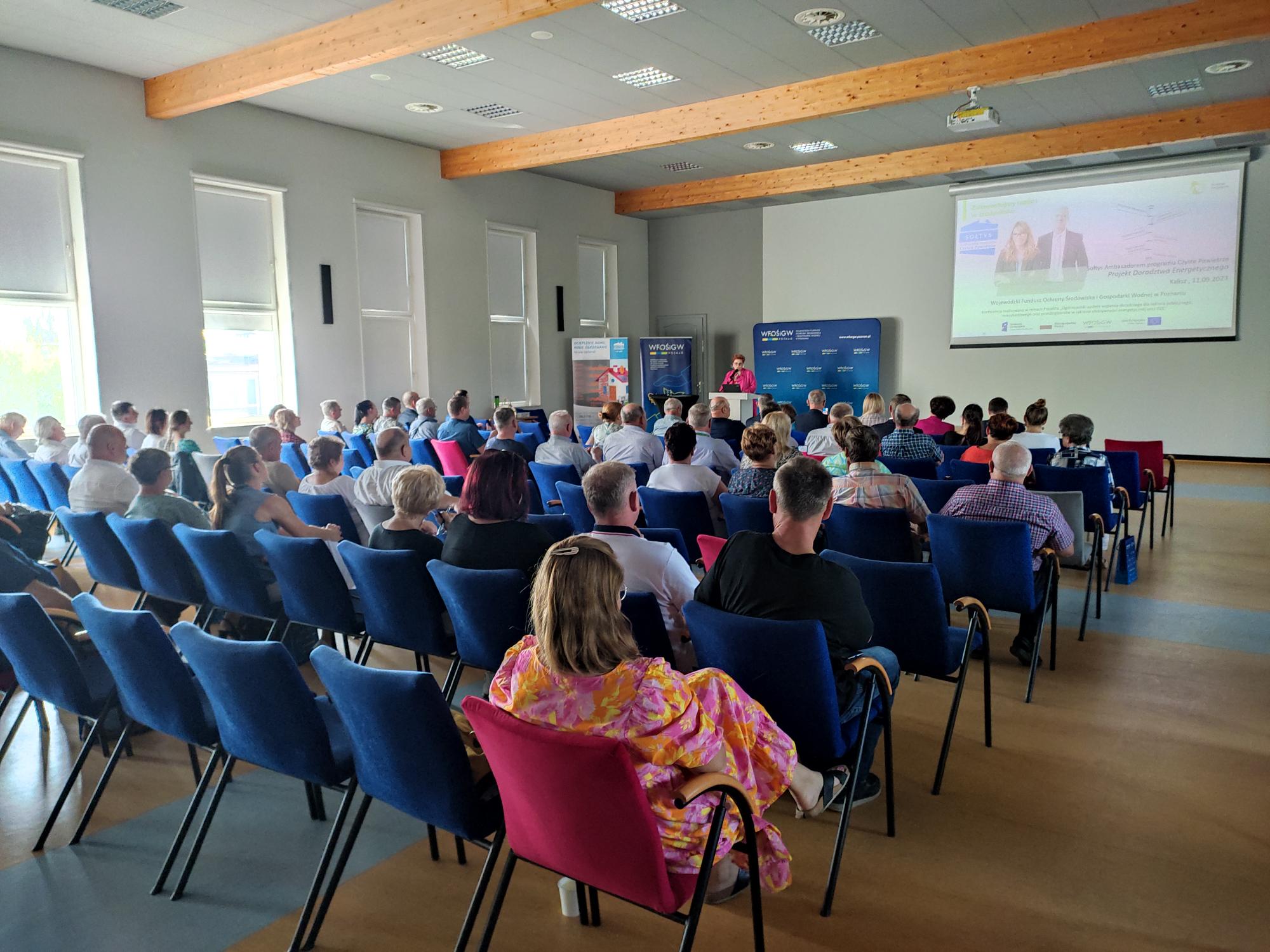 Duża grupa osób siedzi na sali szkoleniowej na krzesłąch.
