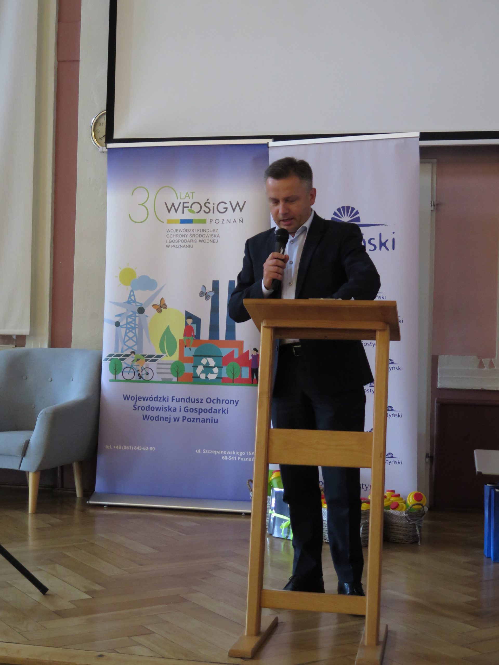 1 osoba stoi na scenie i przemawia.