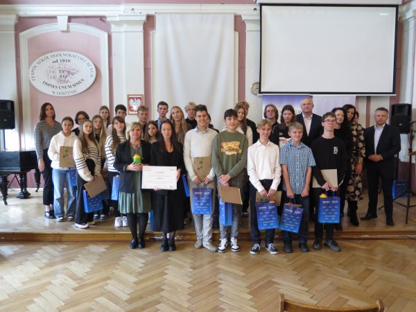 Duża grupa osób stoi na scenie i pozuje do zdjęcia z nagrodą.