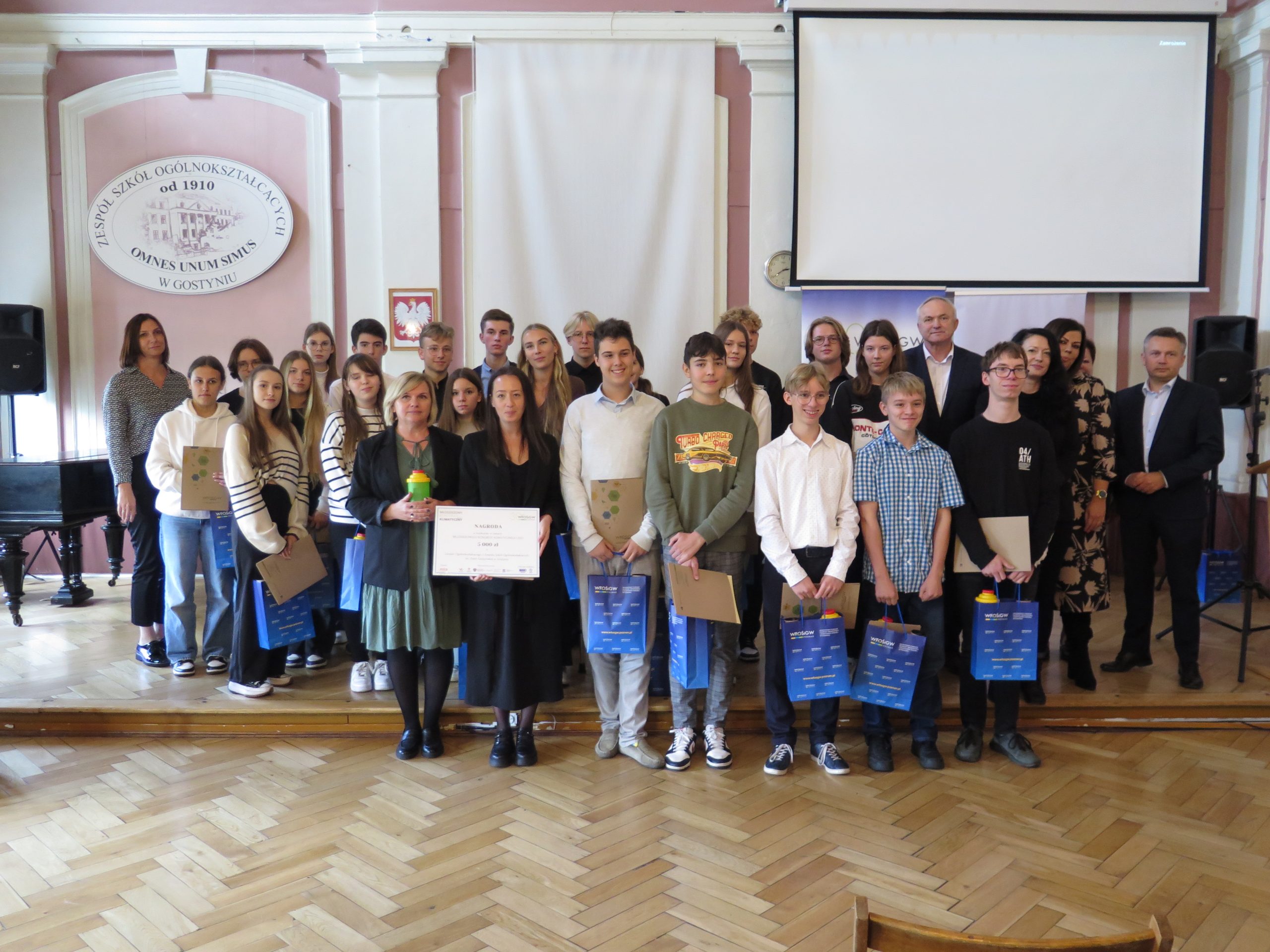 Duża grupa osób stoi na scenie i pozuje do zdjęcia z nagrodą.