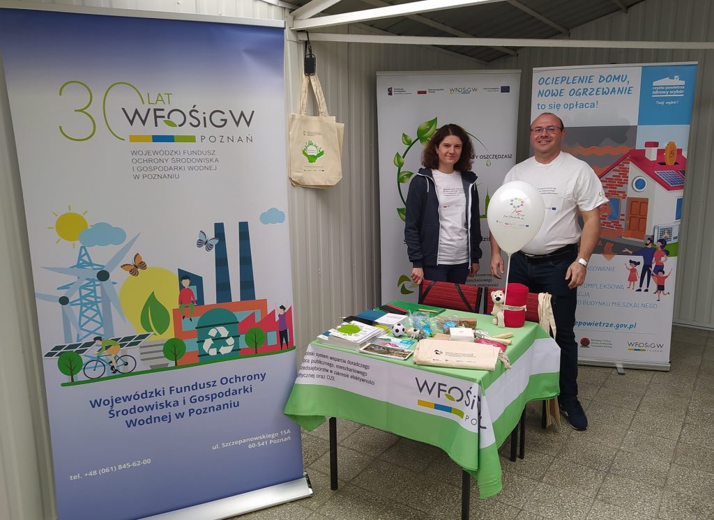 2 osoby stoją na tle bannerów reklamowych i stoiska.