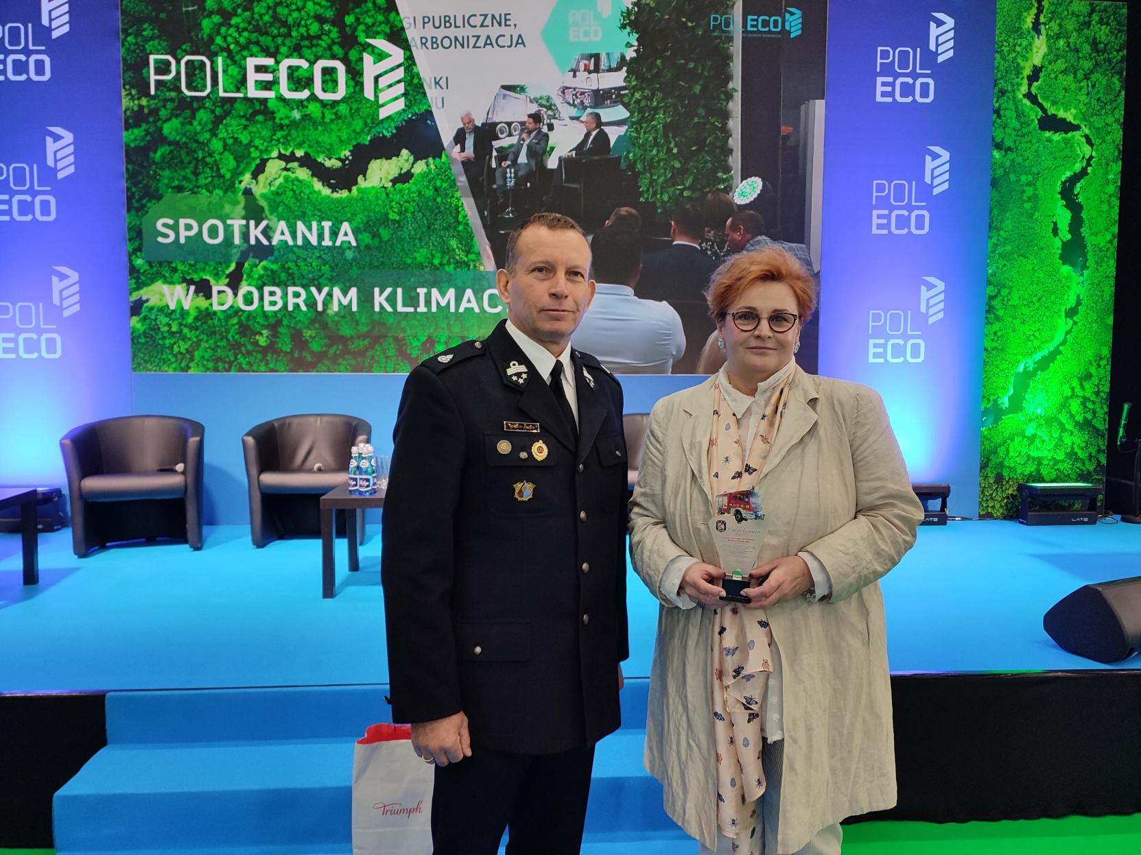 Na tle sceny stoją 2 osoby i pozują do zdjęcia.