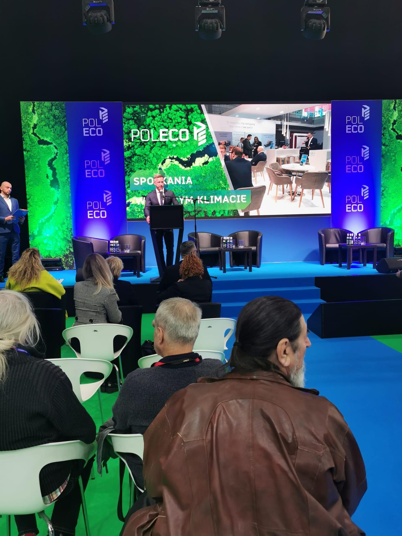 Sala wypełniona ludźmi, na środku jedna osobaprzemawia.