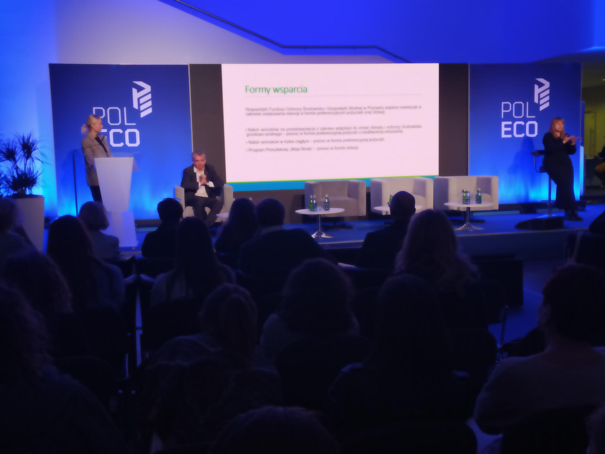 3 osoby siedzą na scenie i debatują podczas konferencji.