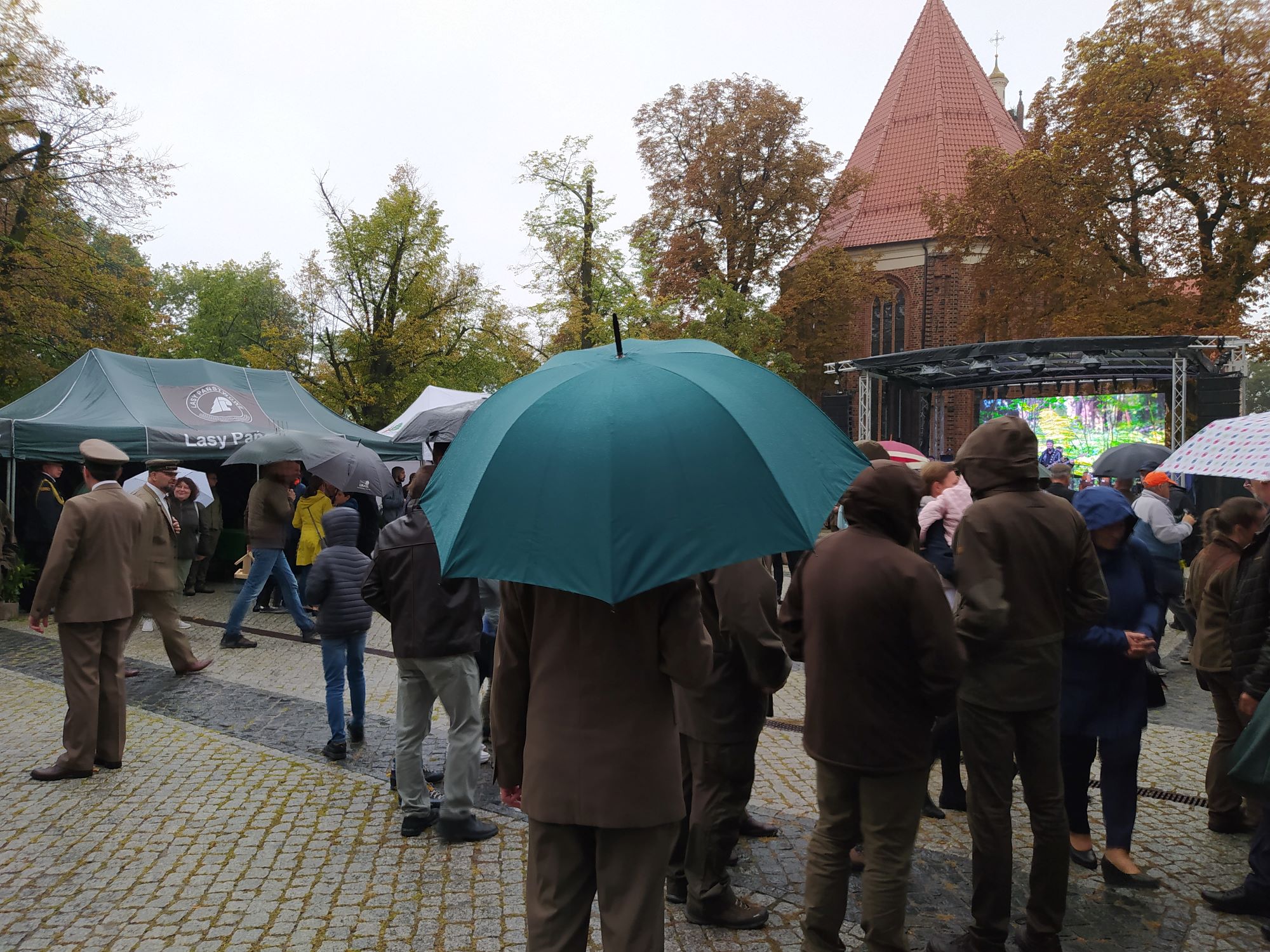 Ludzie zgromadzeni na pikniku, stoją pod parasolami