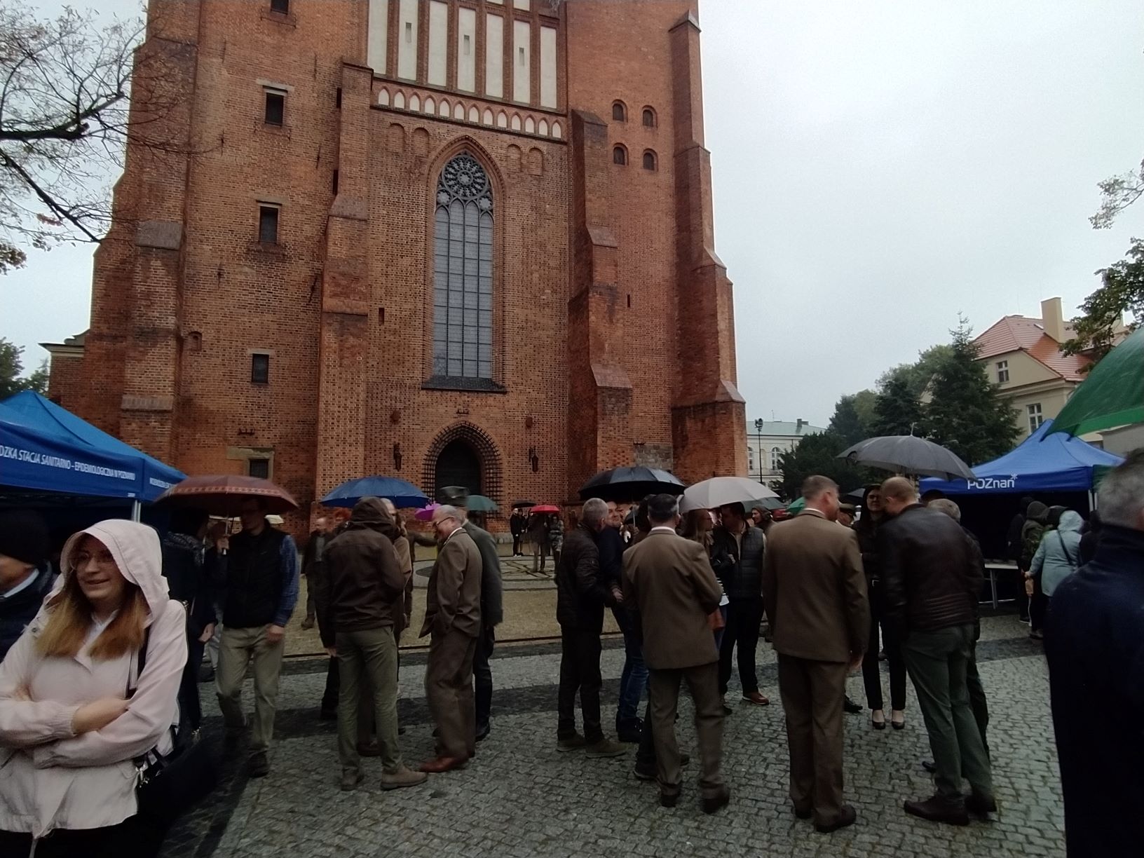 Ludzie zgromadzeni na pikniku, stoją pod parasolami