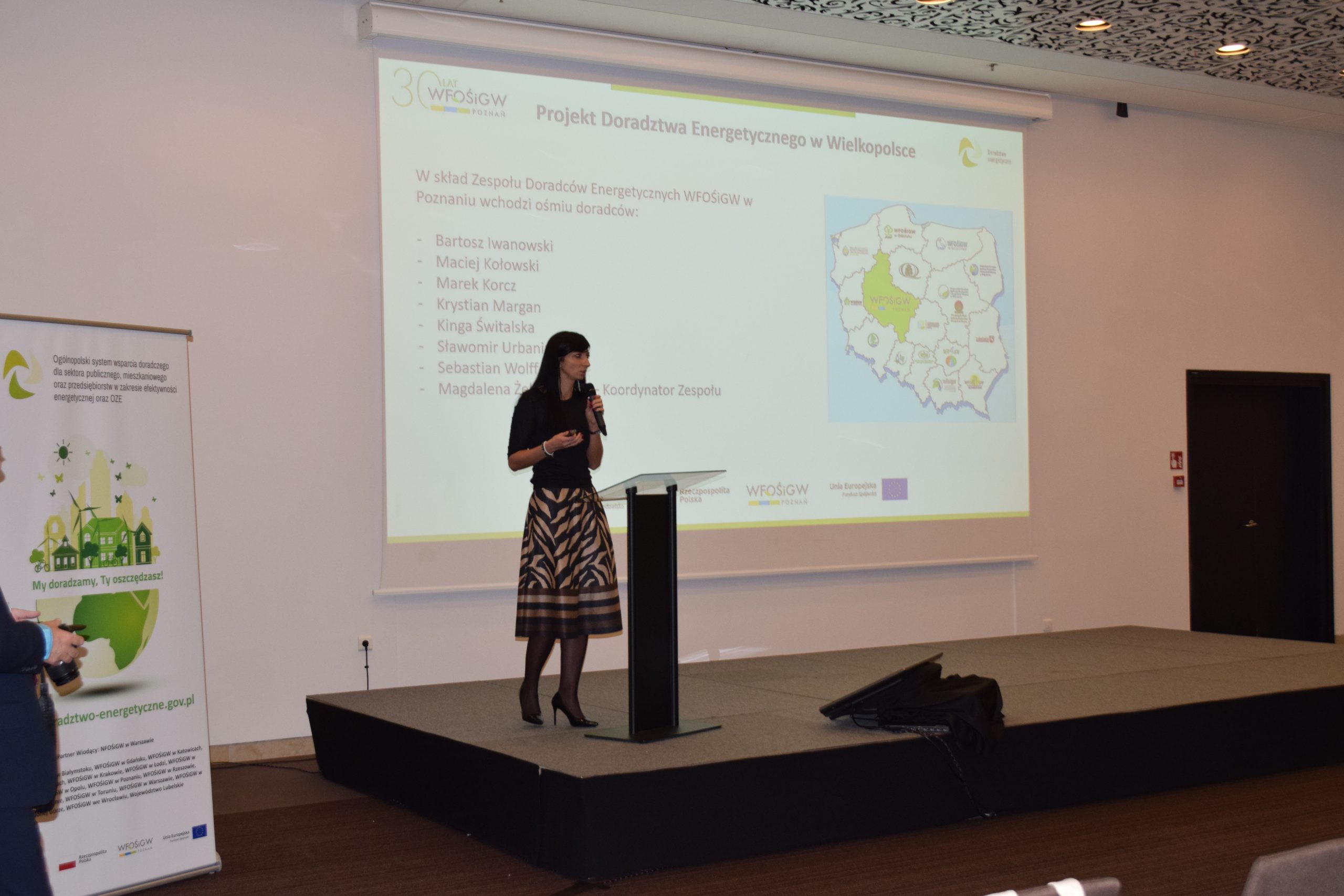 1 osoba stoi na scenie w trakcie konferencji i przemawia do uczestników.