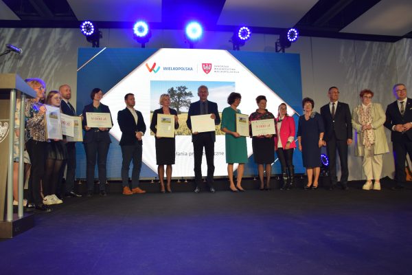 Grupa osób stoi na scenie na tle telebimu i pozuje do zdjęcia.