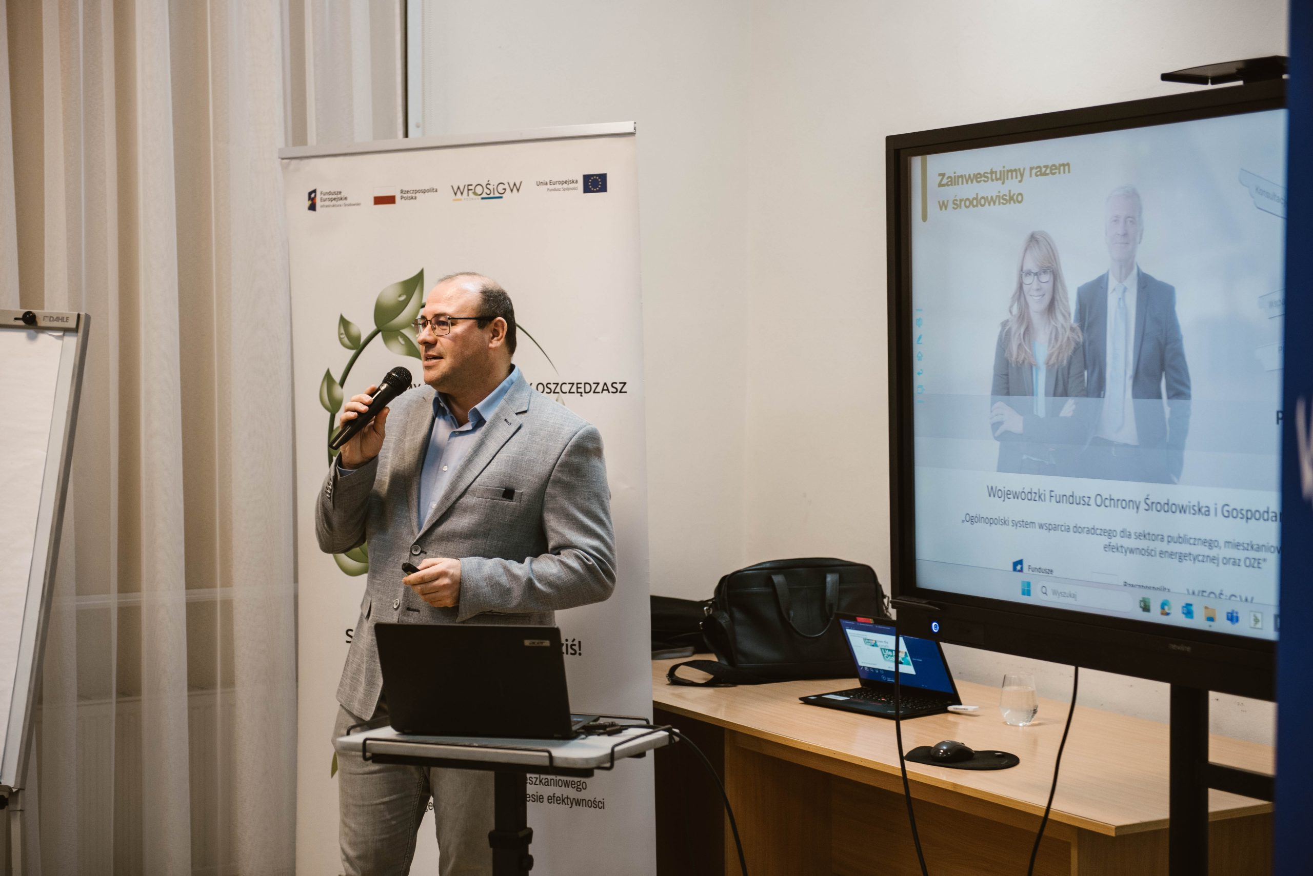 1 osoba stoi na środku sali i przemawia przez mikrofon.