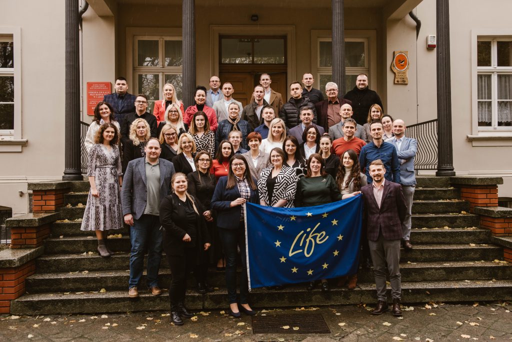 Grupa około 30 osób stoi przed budynkiem i pozuje do zdjęcia