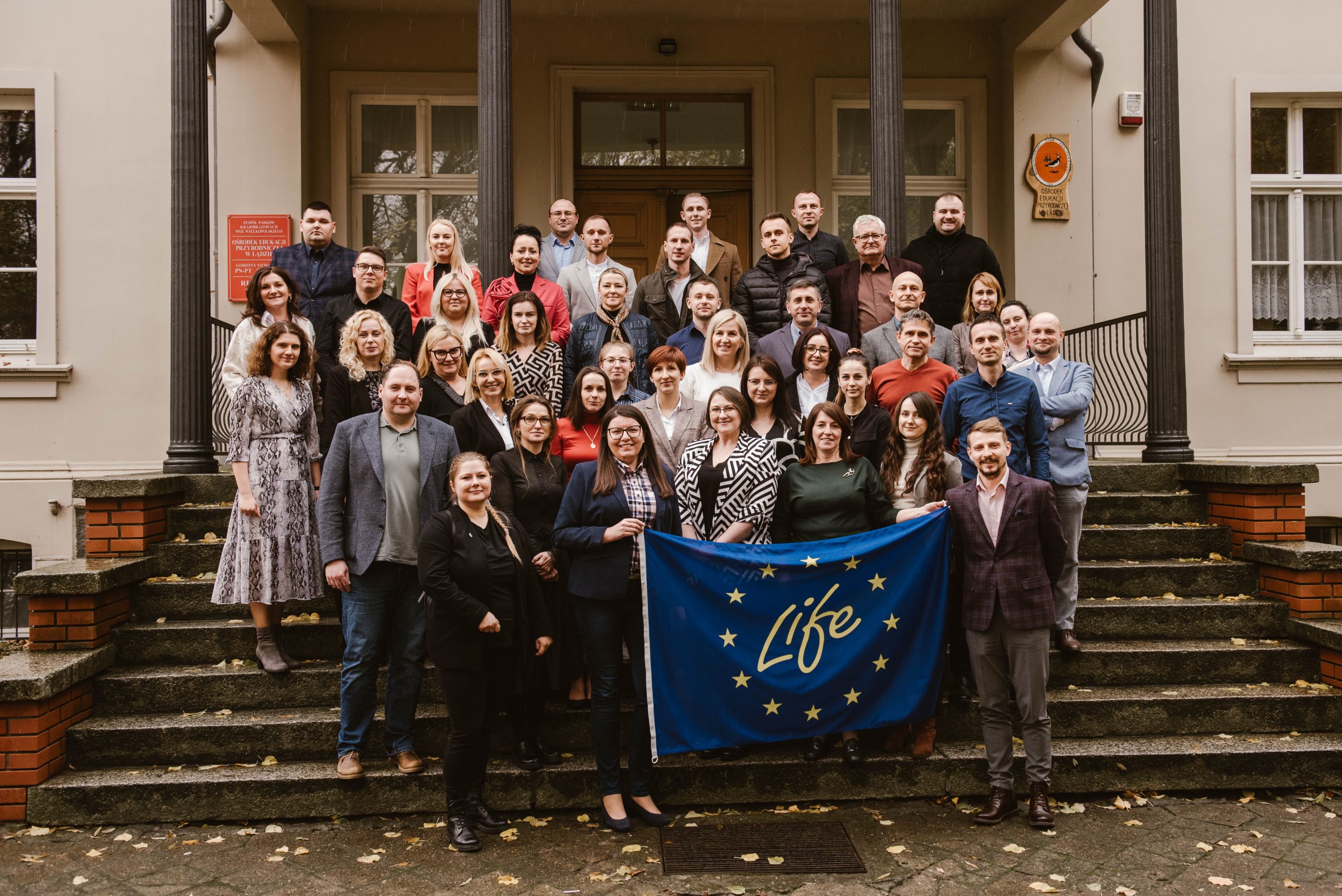 Grupa około 30 osób stoi przed budynkiem i pozuje do zdjęcia