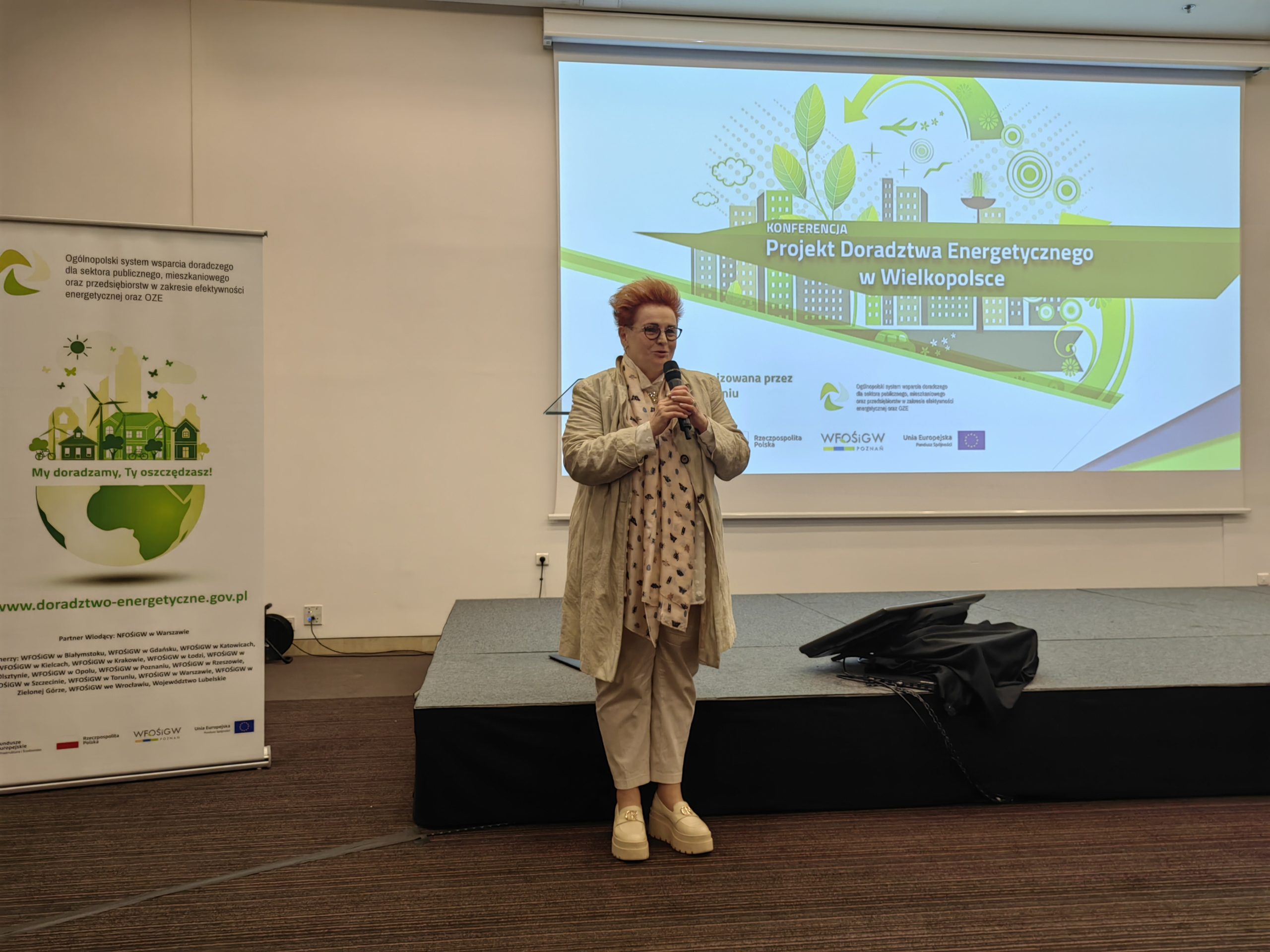 1 osoba stoi na scenie w trakcie konferencji i przemawia do uczestników.