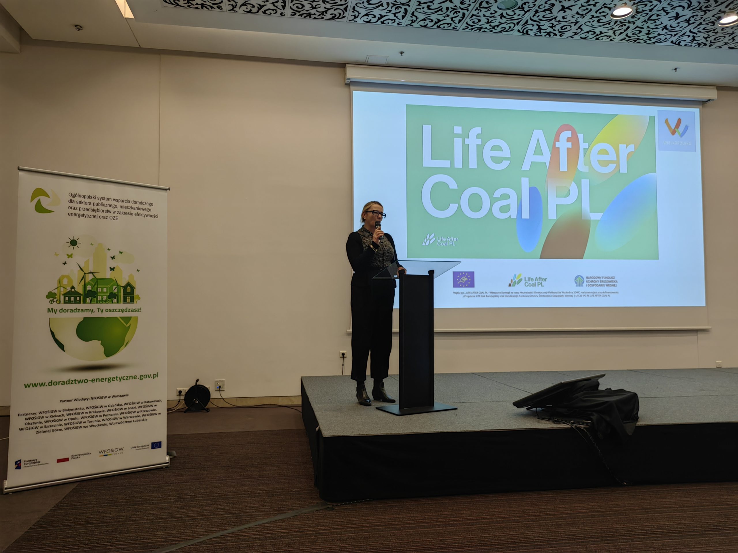 1 osoba stoi na scenie w trakcie konferencji i przemawia do uczestników.