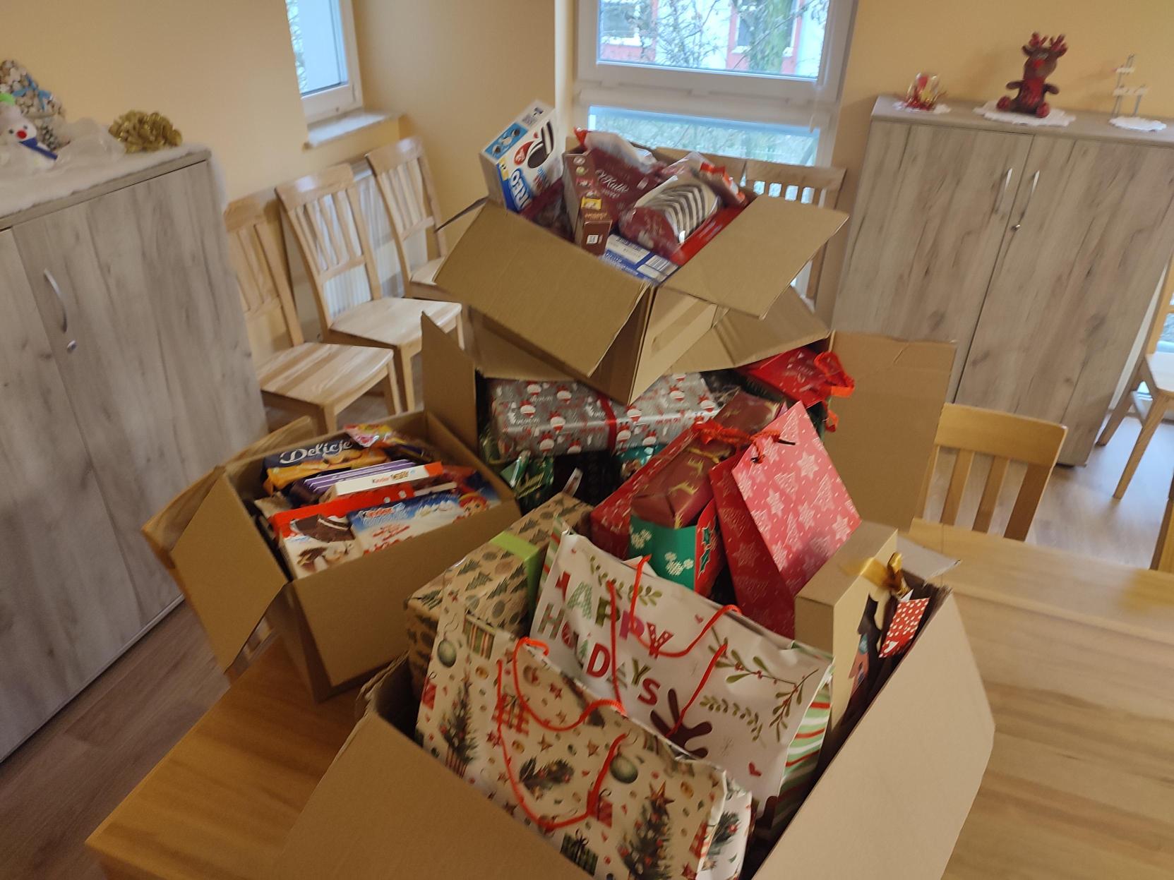 W świetlicy w domu dziecka na stole stoja kartony z zapakowanymi prezentami dla dzieci oraz słodycze.