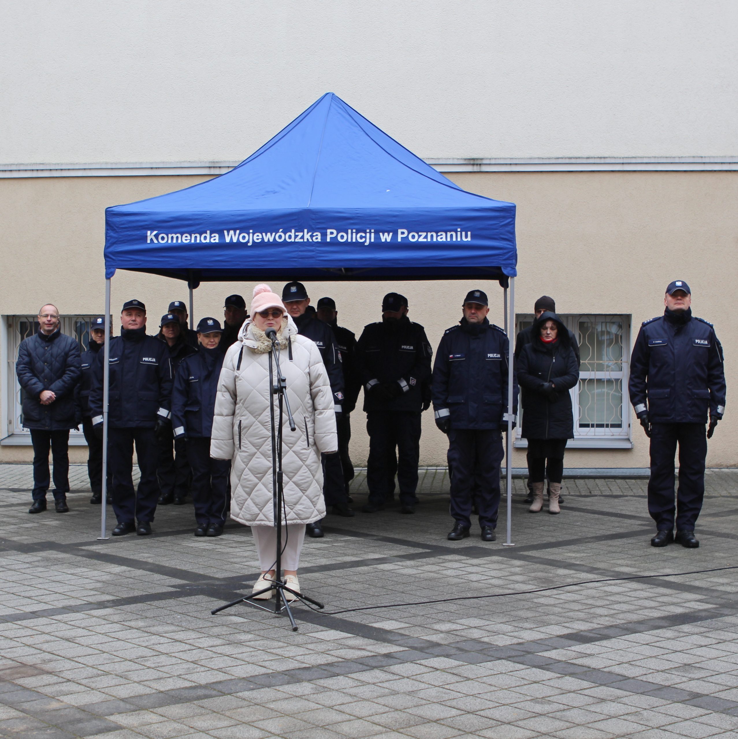 Goście zaproszeni na uroczystość przekazania samochodów bojowych dla Komendy Wojewódzkiej w Poznaniu, stoją pod namiotem na dziedzińcu podczas uroczystości, przemawia Prezes Zarządu WFOŚiGW w Poznaniu.