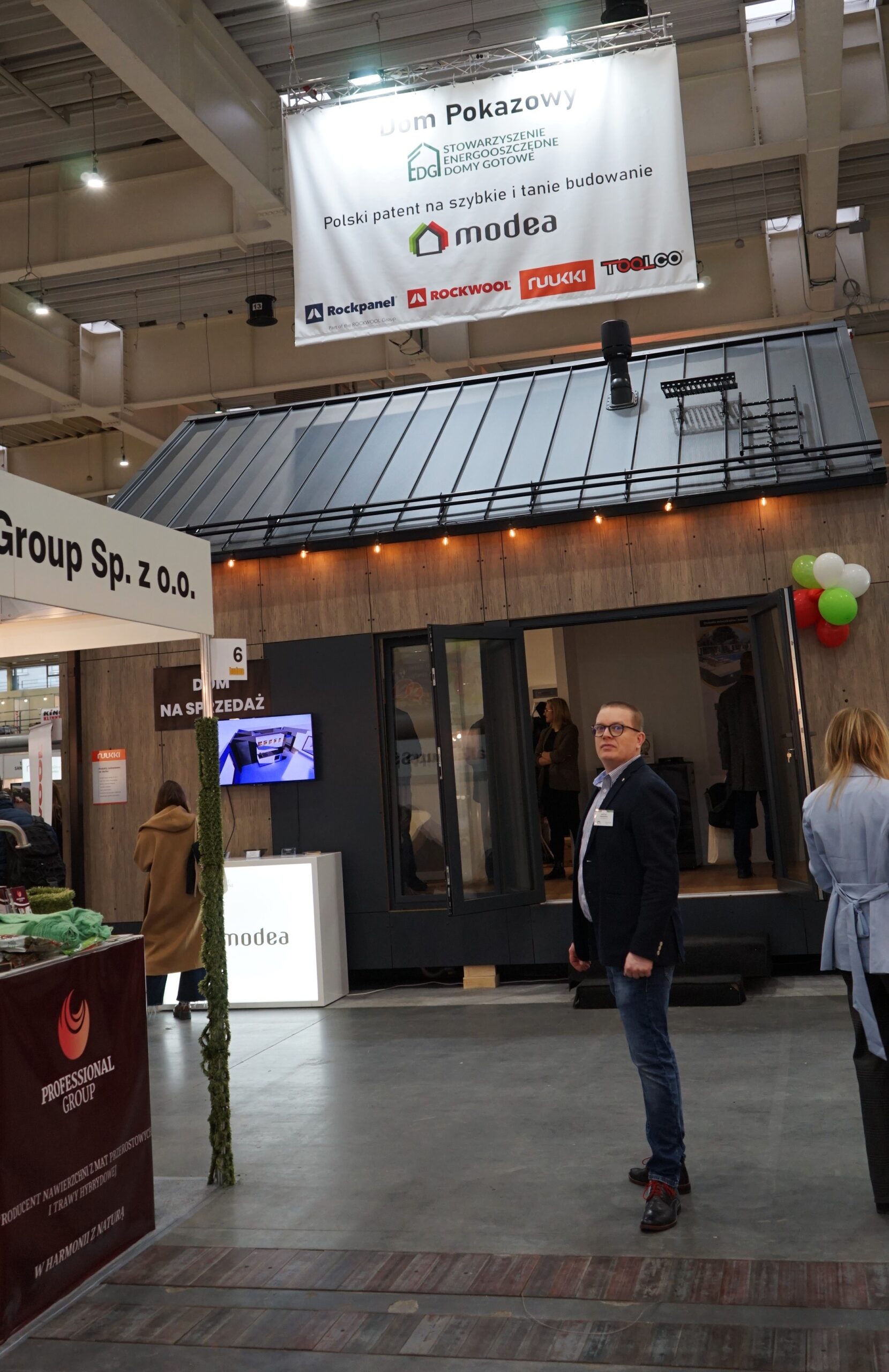 Widok hali targowej, jedna osoba stoi na tle ściany i stoisk