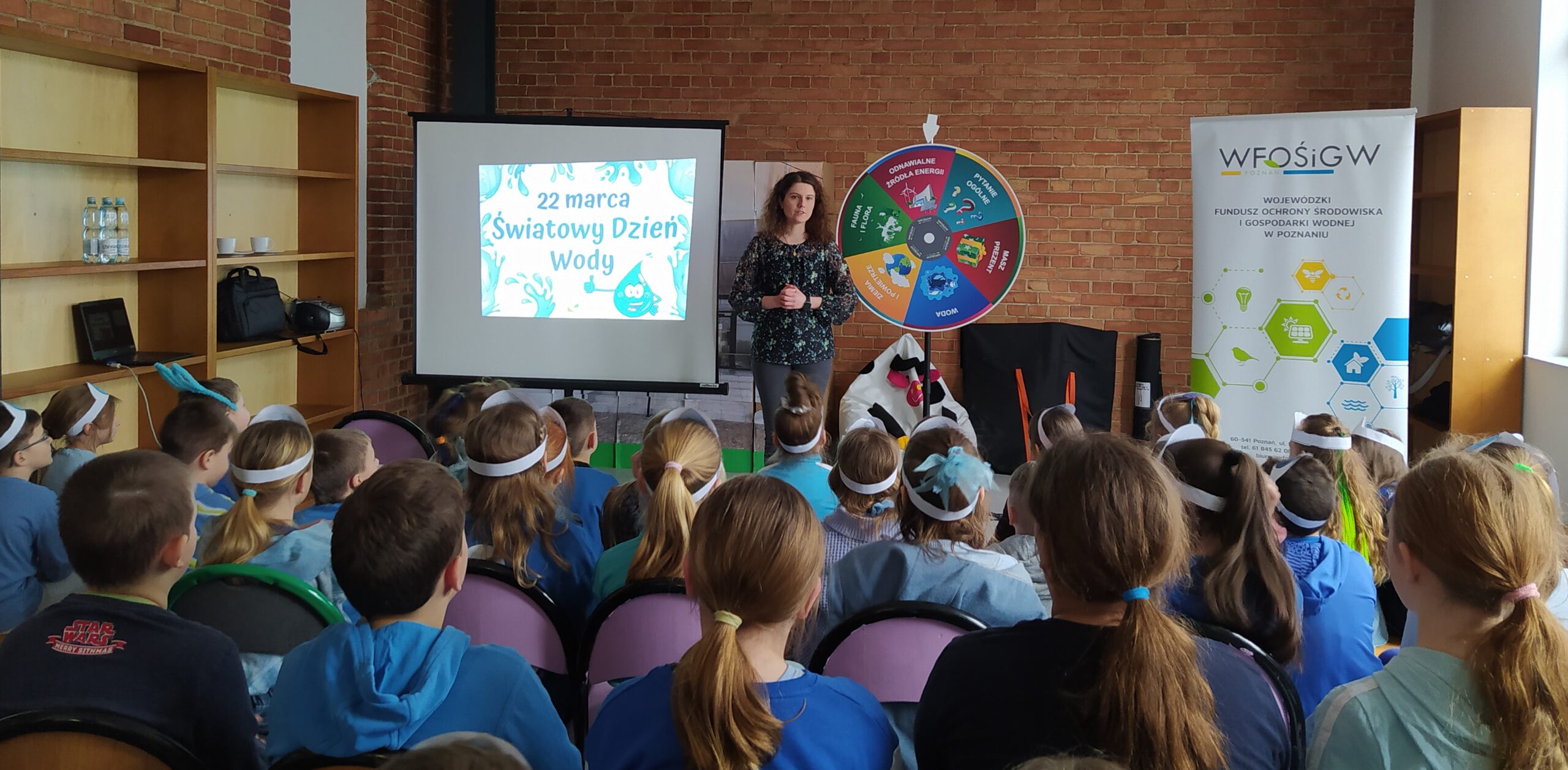 W sali w Sp w Drawsku dzieci siedzą na krzesełkach i słuchają prelekcji prowadzonej przez doradców klimatyczno-energetycznych z WFOŚiGW w Poznaniu.