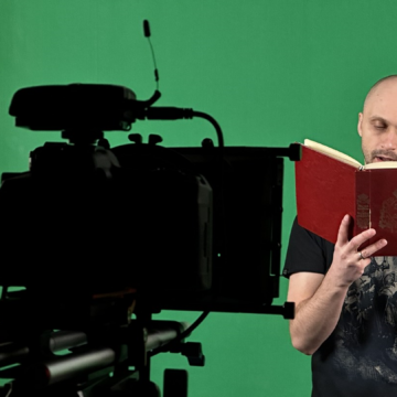 Jedna osoba stoi na tle zielonej ściany i czyta z książki przed kamerą, która nagrywa.
