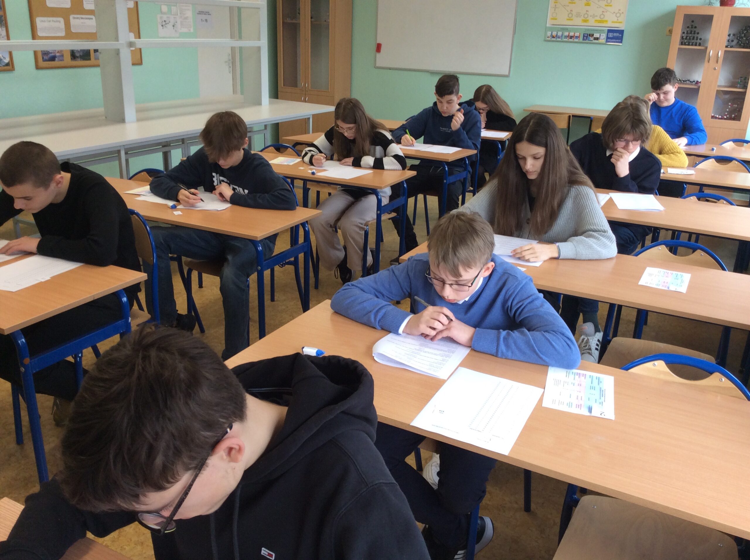 Uczniowie siedzą w ławkach i piszą test konkursowy.