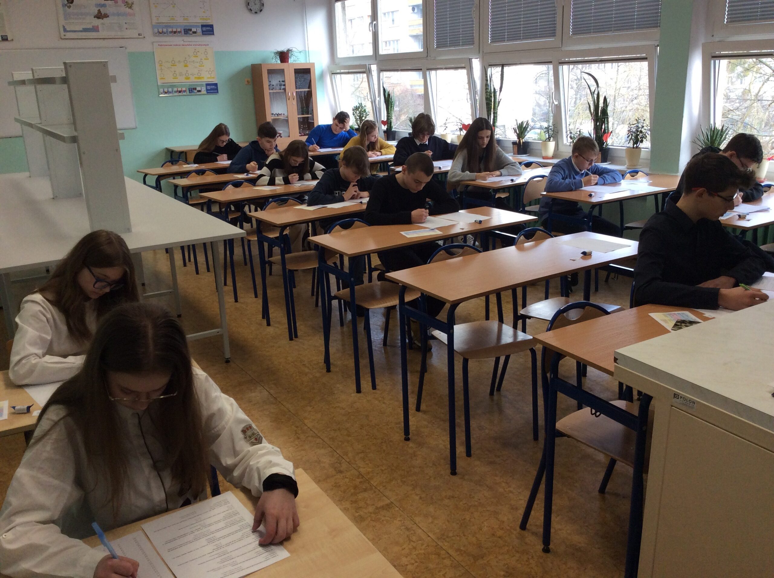 Uczniowie siedzą w ławkach i piszą test konkursowy.