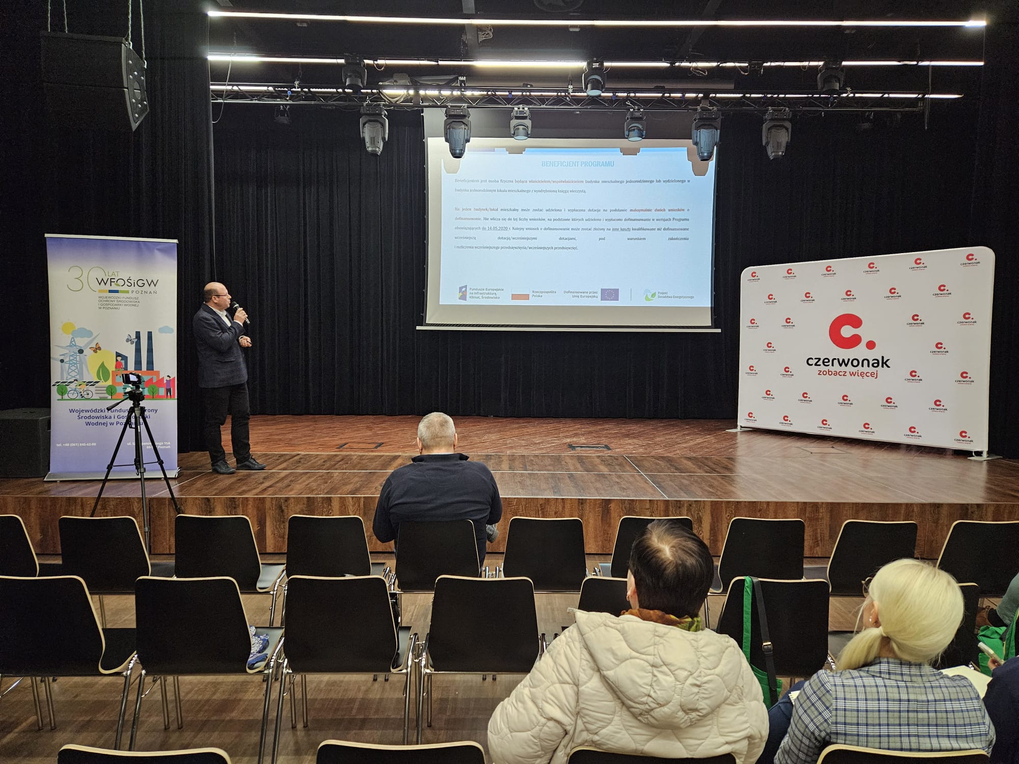 Salawypełniona ludźmi i doradca WFOŚiGW w Poznaniu przedstawia prezentację stojąc na środku sali przed rzędami krzeseł.