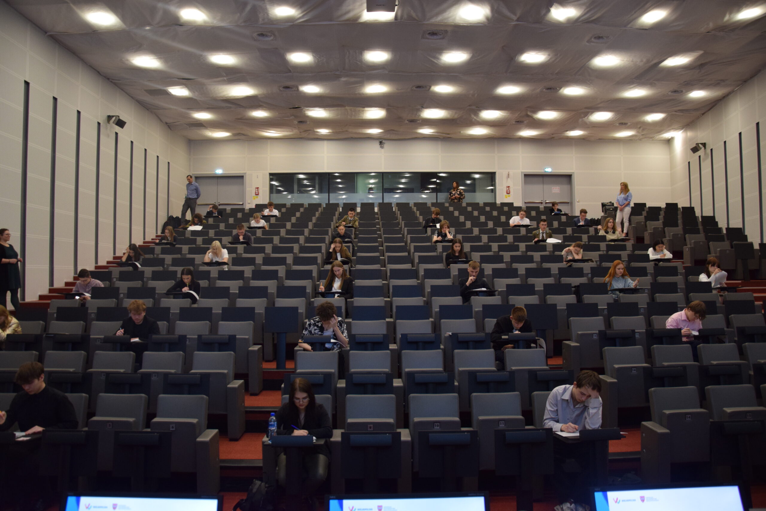 Widok na salę i siedzących uczniów piszących pisemną część olimpiady.