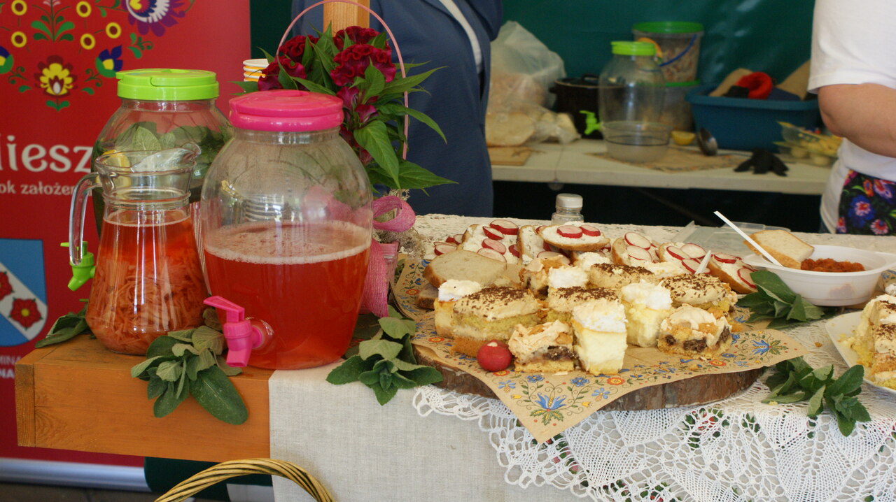 Zdjęcie przedstawia stół z lokalnymi specjałami kuchni - tutaj różnego rodzaju ciasta pokrojone na kawałki oraz słoik z lemoniadą.