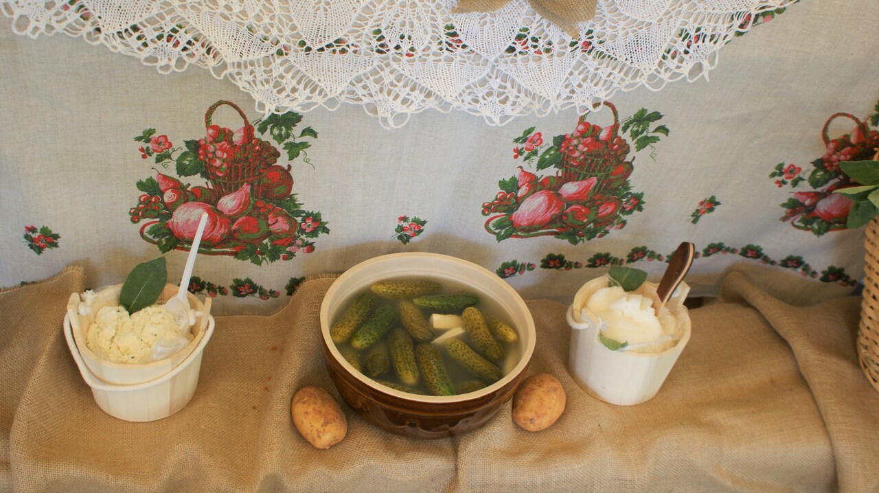 Zdjęcie przedstawia stół z lokalnymi specjałami kuchno - tutaj kamionkowy garnek z kiszonymi ogórkami.