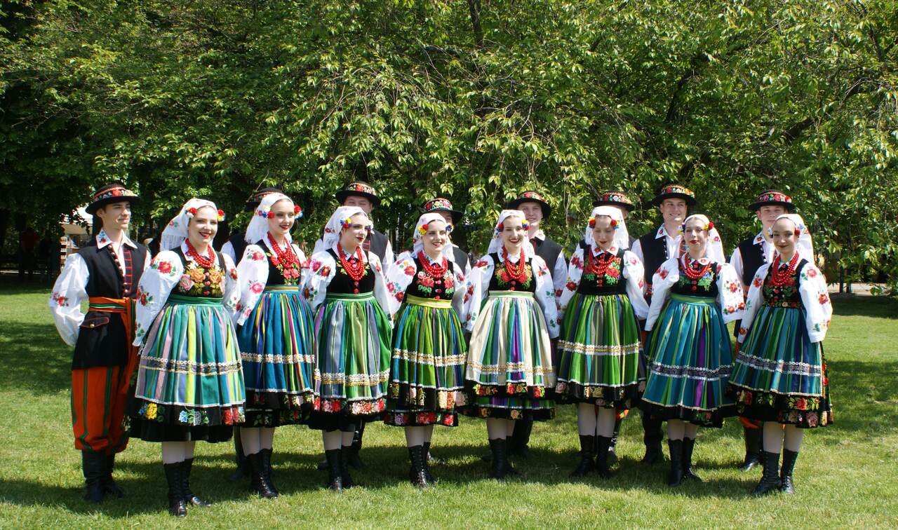 Zdjęcie przedstawia zespół muzyczny folklorystyczny, który będzie występował na festynie. Panie stoją w pierwszym rzędzie, a za nimi panowie, wszyscy ubrani w stroje tradycyjne.