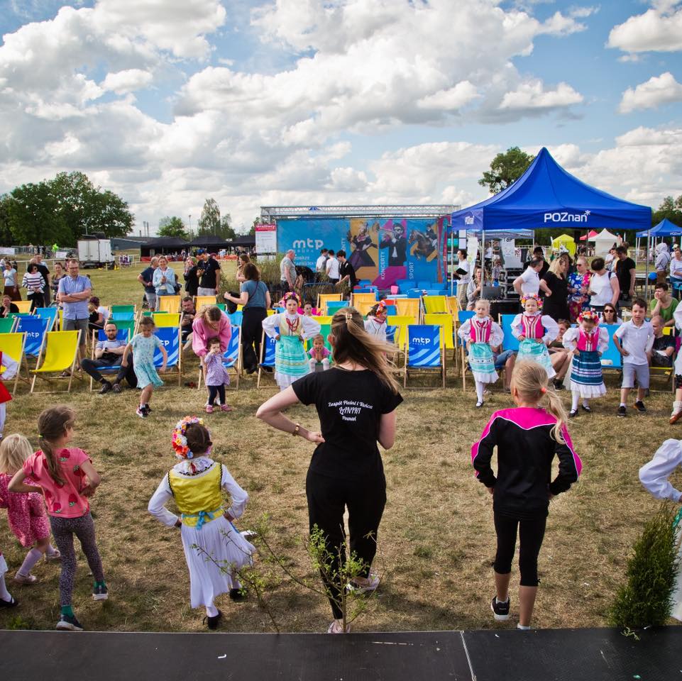 Zdjęcie przedstawia teren wydarzenia plenerowego na trawie, gdzie odbywają się ćwiczenia - 3 osoby pokazują ćwiczenie, a ludzie stojący naprzeciwko wykonują ćwiczenia.