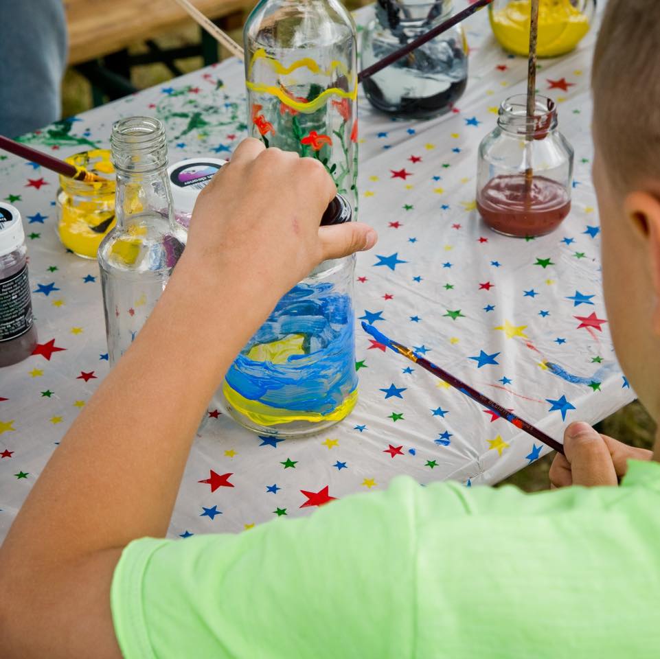 Zdjęcie przedstawia malowany słoik na warsztatach plastycznych, widać dziecięcą rączkę, która farbami maluje słoik.