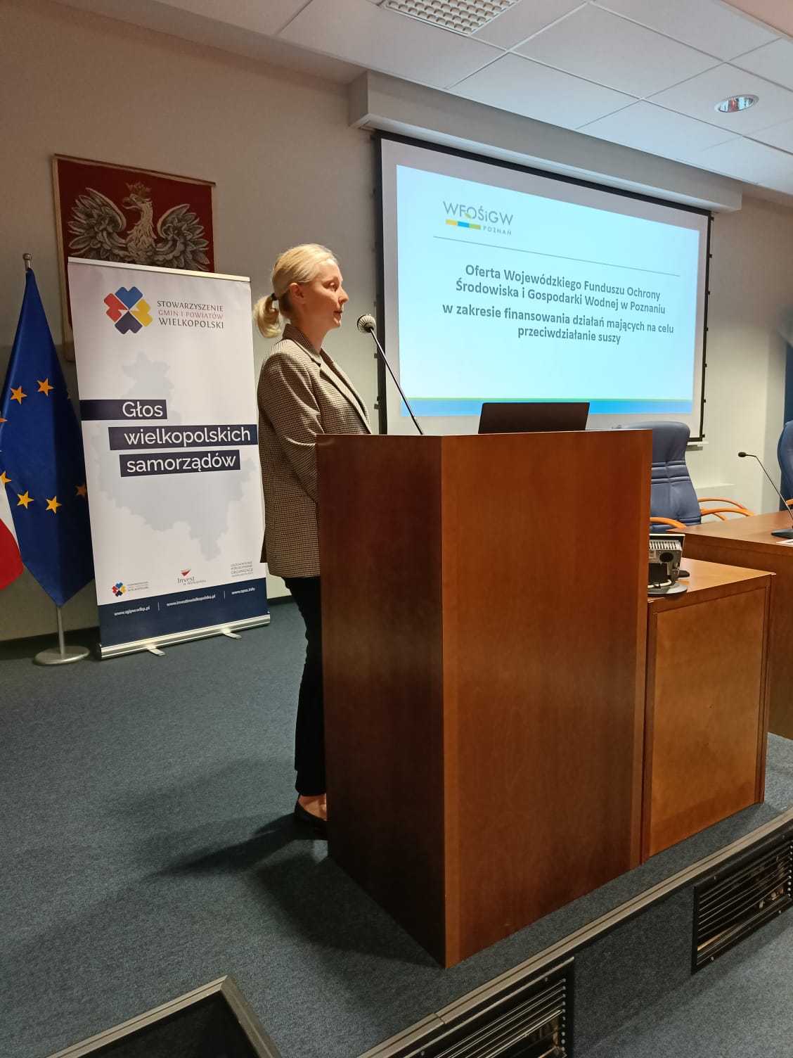 Anna Romanowska z WFOŚiGW w Poznaniu, stoi na scenie, na tle wyświetlanej prezentacji i przedstawia prelekcję.