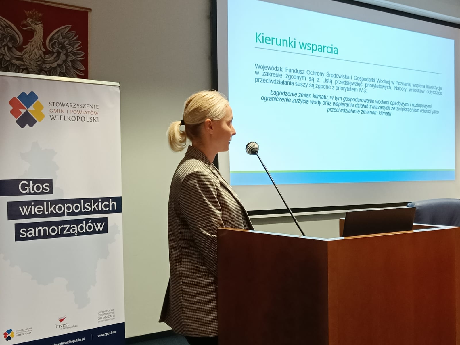 Anna Romanowska z WFOŚiGW w Poznaniu, stoi na scenie, na tle wyświetlanej prezentacji i przedstawia prelekcję.