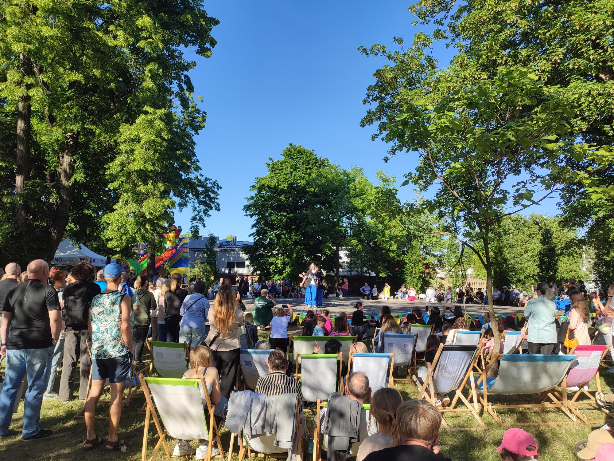 Park, na środku scena, wokół sceny dużo ludzi stojących wokół sceny i siedzących na leżakach.