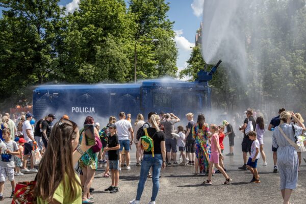 Na placu stoi policyjna armatka woda i leje się w górę woda, wokół stoją ludzie i oglądają pokaz.