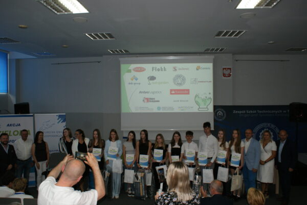 18 osób stoi na scenie po wręczeniu nagród.