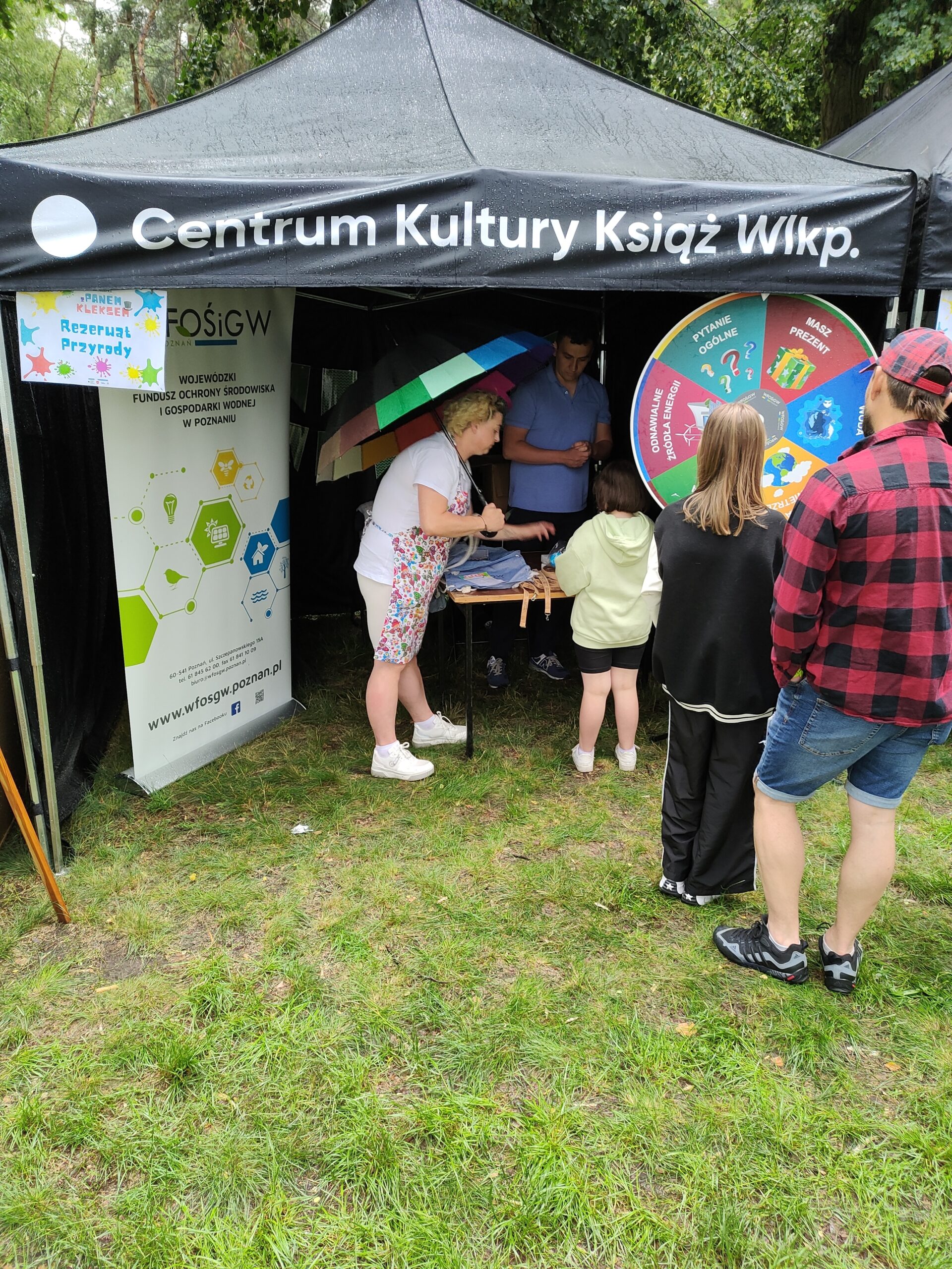 Namiot podczas festynu, a w jego okolicy stoi kilka osób.