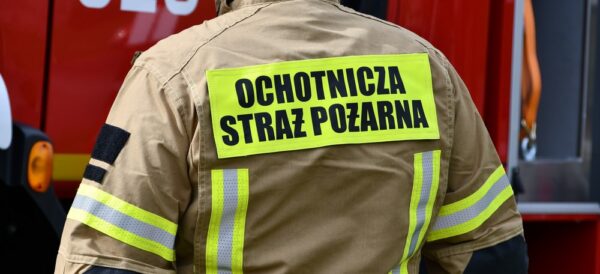Na zdjęciu druh z Ochotniczej Straży Pożarnej, stojący tyłem, na plecach na mundurze widnieje napis: "Ochotnicza Straż Pożarna".