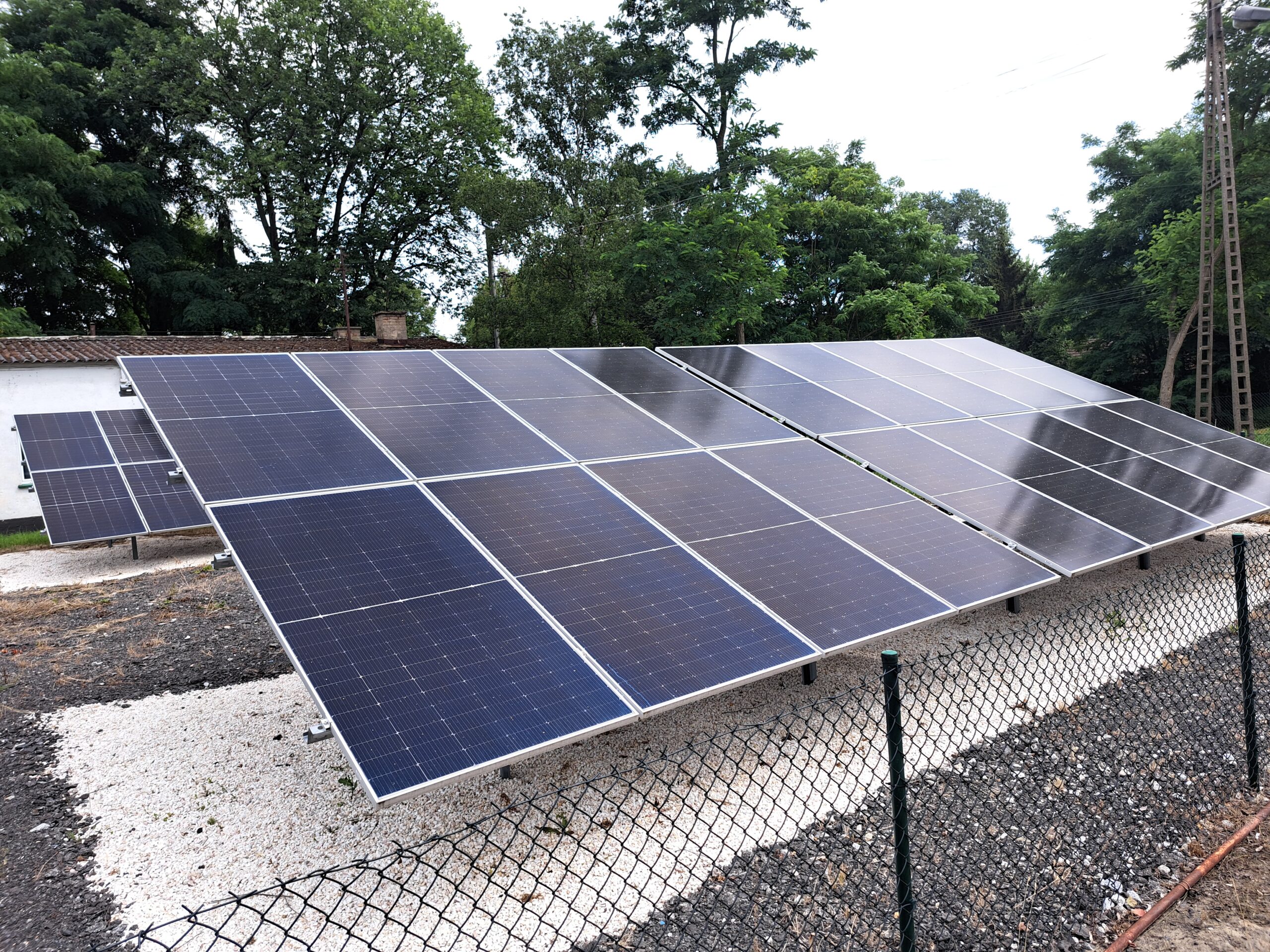 Zdjęcie przedstawia panele fotowoltaiczne na zewnątrz spółdzielni energetycznej na wydzielonym terenie ogrodzonym płotem.