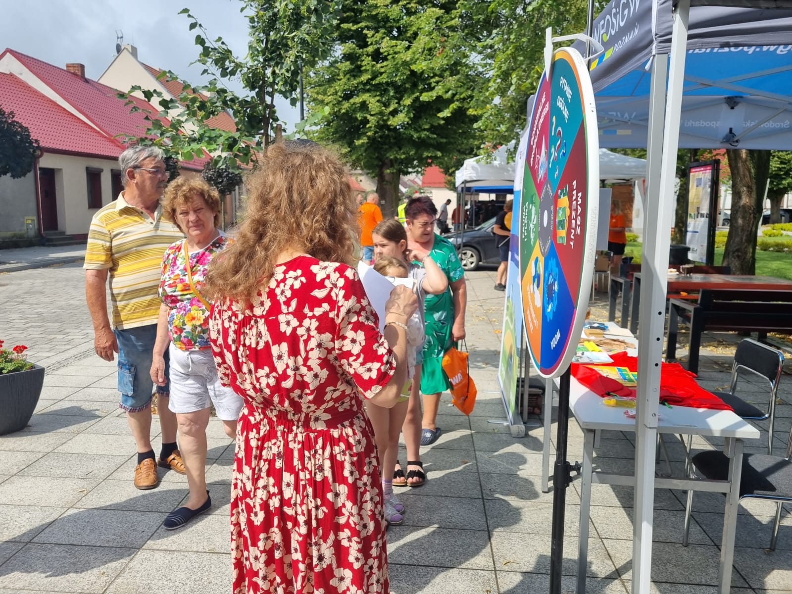 Zdjęcie przedstawia widok stoiska WFOŚiGW w Poznaniu i dzieci biorące udział w kole fortuny.