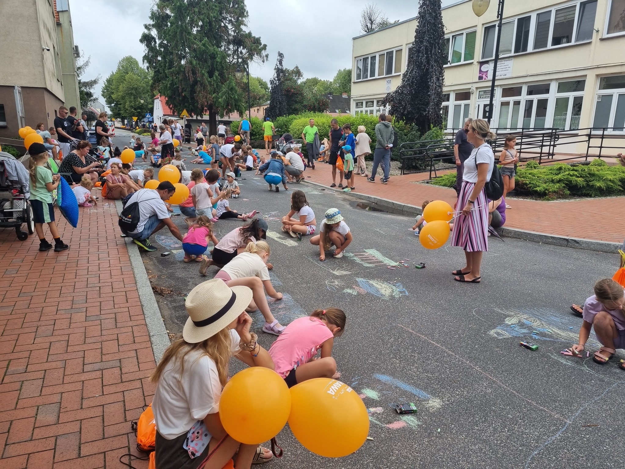 Uliczka, na której mnóstwo dzieci rysuje kolorowymikredami.