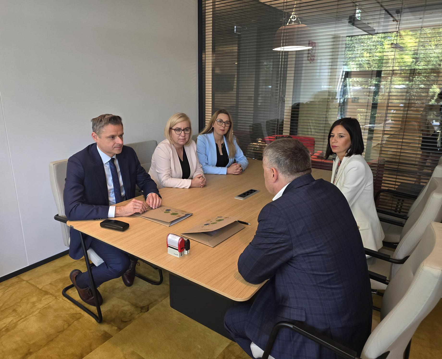 5 osób siedzi przy stole i podpisuje umowę.