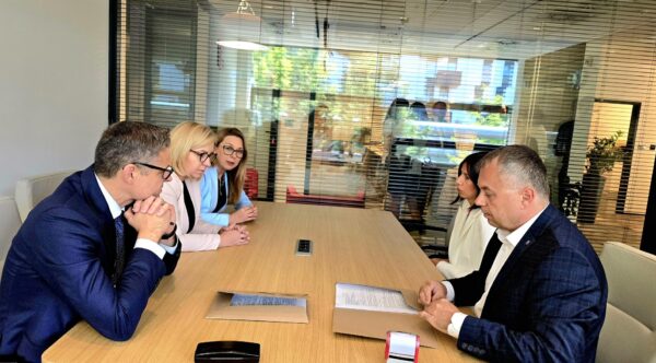 5 osób siedzi przy stole i podpisuje umowę.