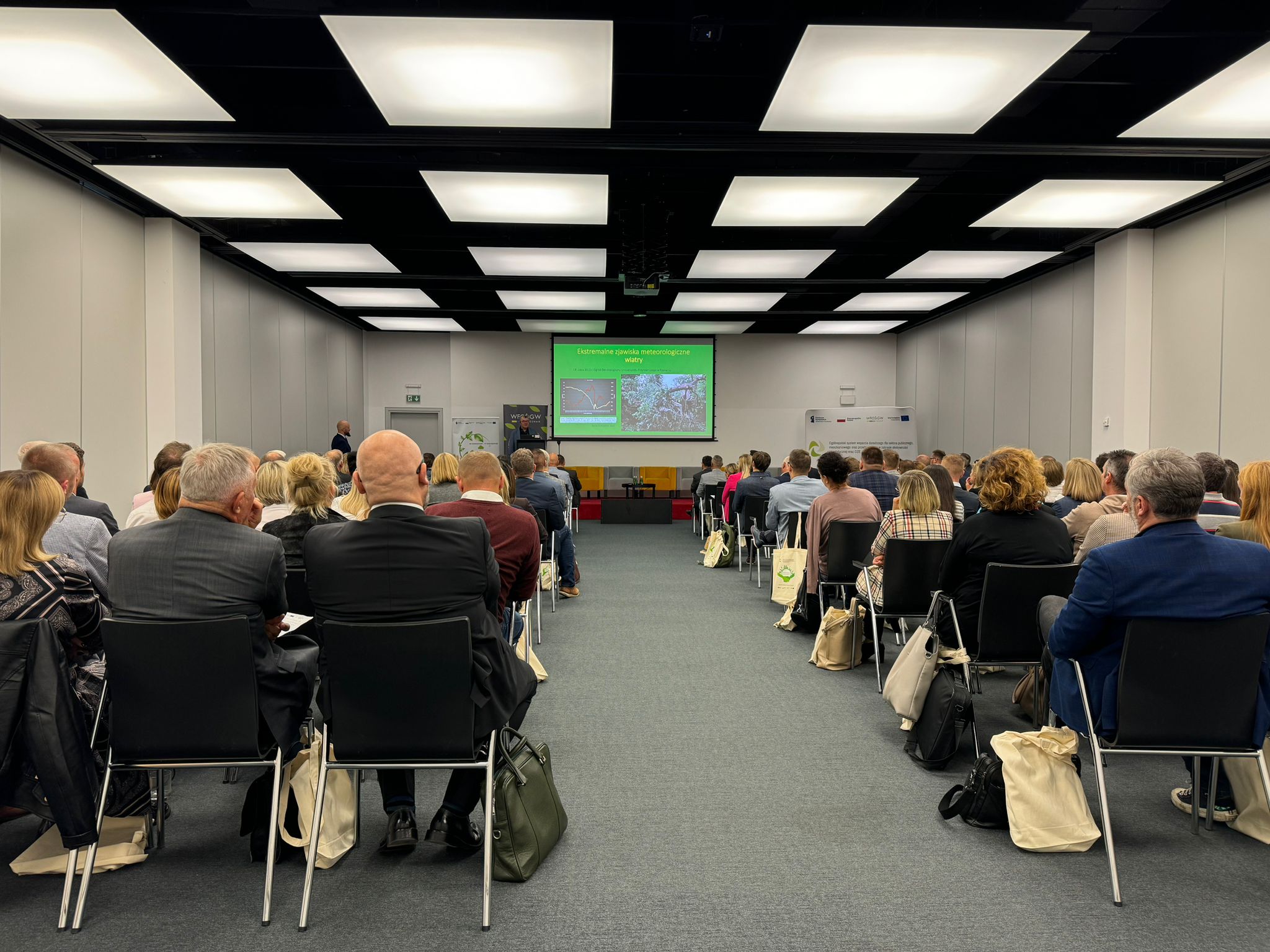 Widok na sale na konferencji z siedzącymi na krzesłach uczestnikami.