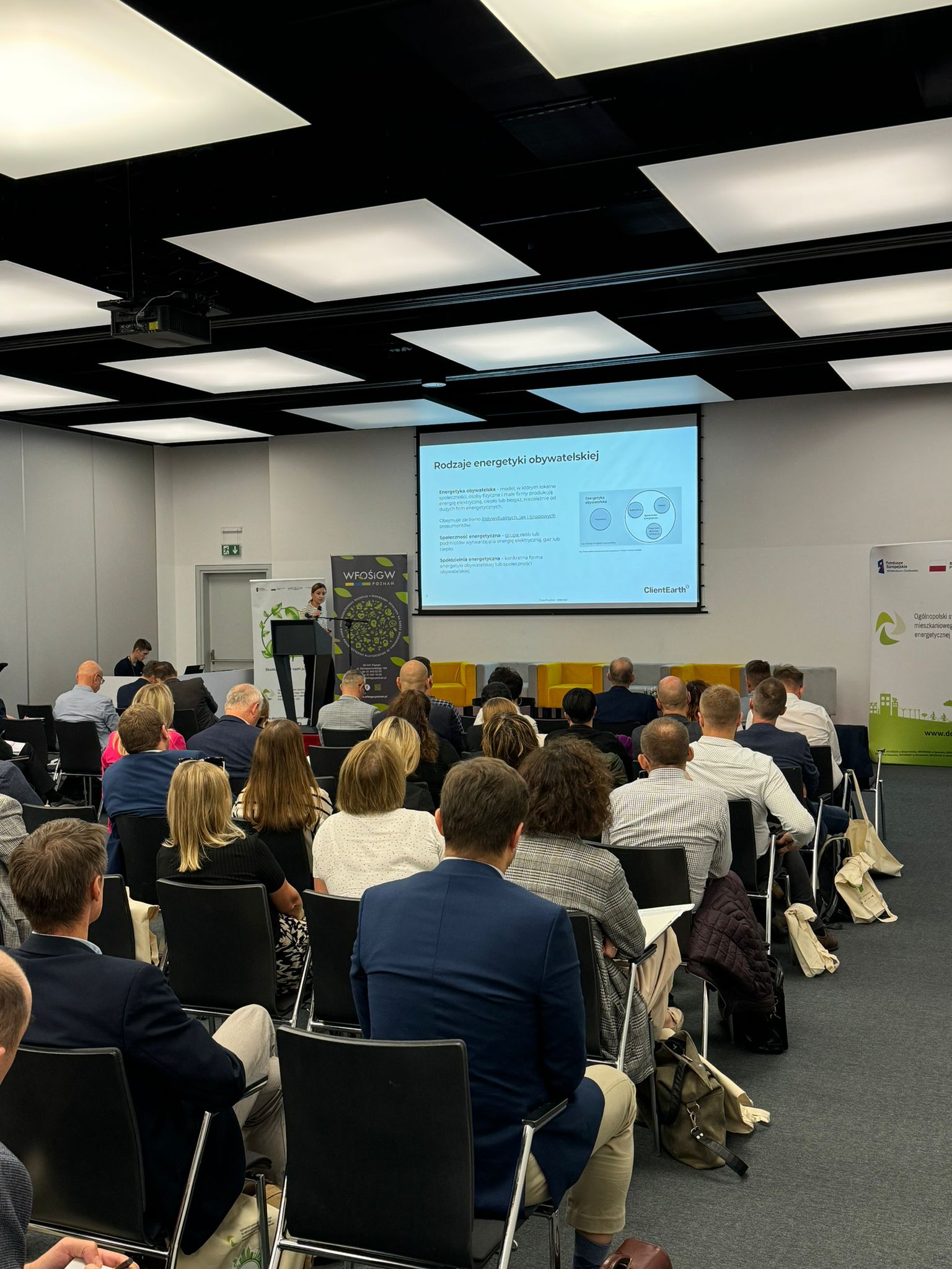 Sala wypełniona uczestnikami konferencji, a na scenie prelegent omawia prezentację.