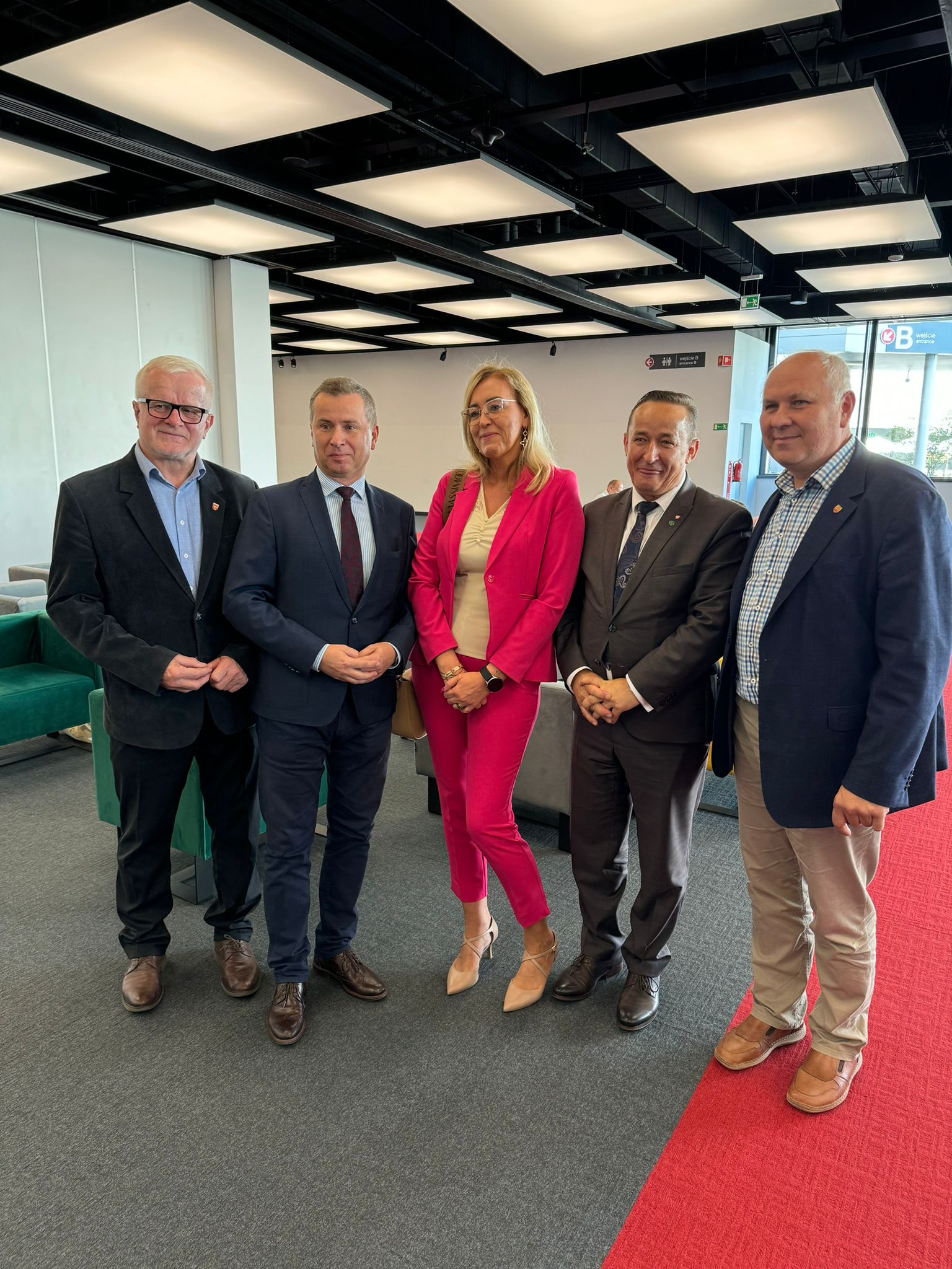 4 osoby stoją w hallu przed salą konferencyjną i pozują do zdjęcia.