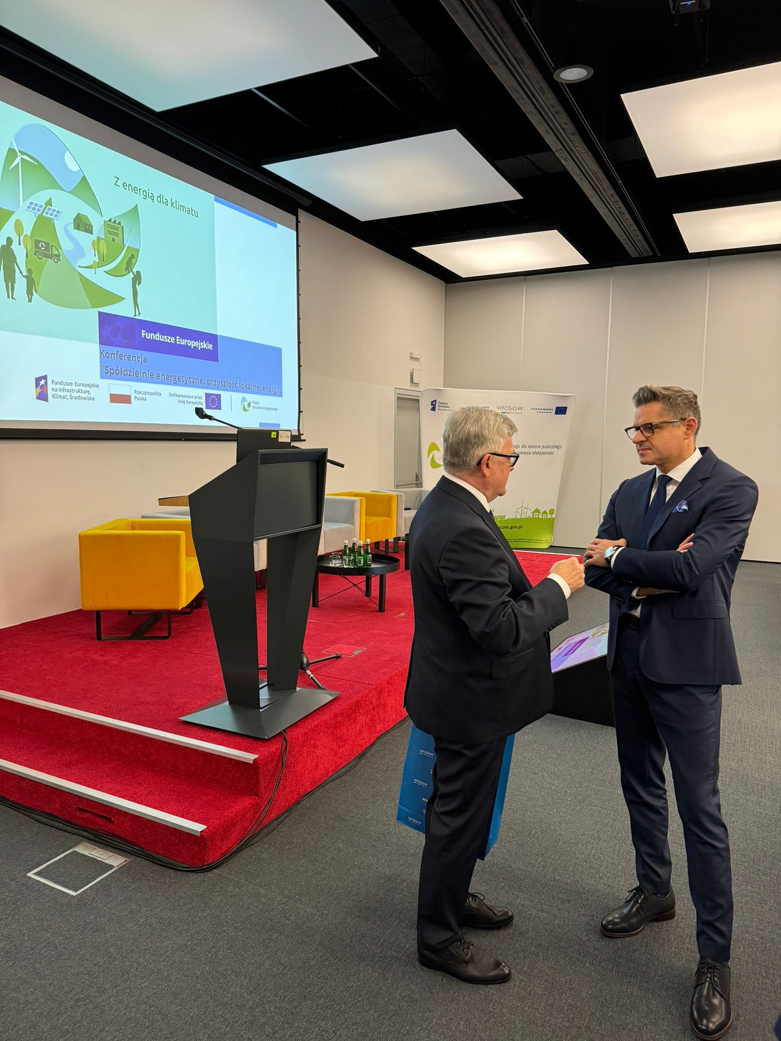 2 osoby stoją przed sceną podczas przerwy i rozmawiają.