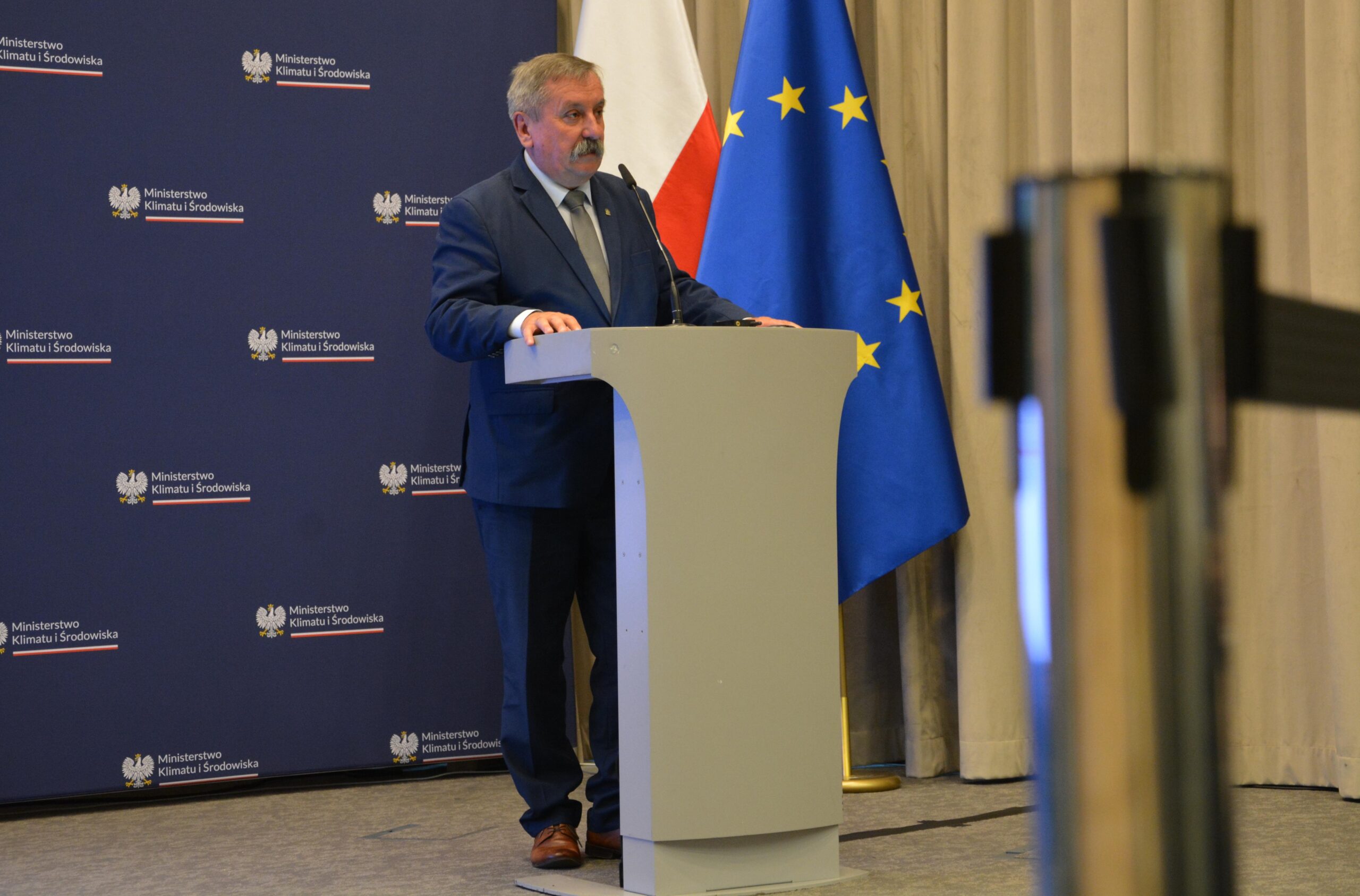 Jedna osoba stoi za mównicą i przemawia.